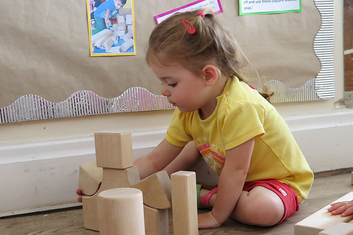 Girl sitting on the ground is building a tower out of wooden blocks