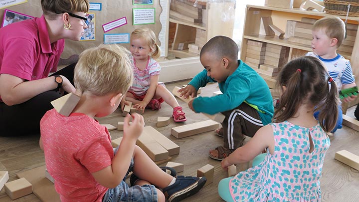 A group of children is playing with wooden blocks with their teacher