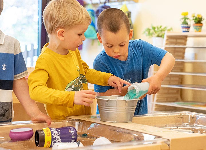 Two young boys are pouring water at an indoor sand and water table