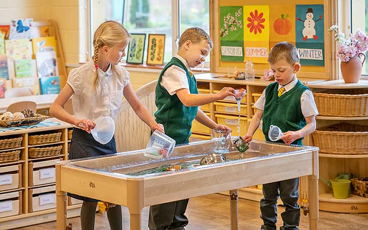 Three six-year old children are playing and experimenting with an indoor sand and water table