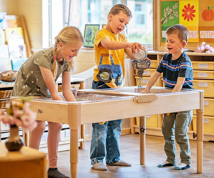 Three six-year old children are playing and experimenting with an indoor sand and water table