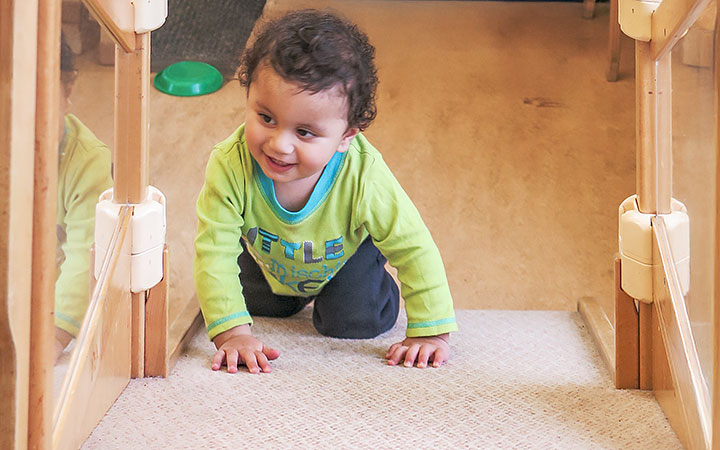 A baby wearing a green shirt and crawling up a nursery gym ramp