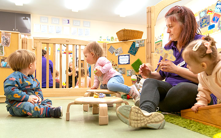 A group of three babies with a teacher in an enclosed baby area
