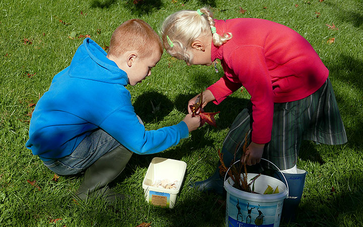 Two children collecting leaves in buckets