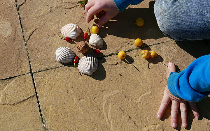 child’s hands arranging pattern with seashells, rosehips and crab-apples