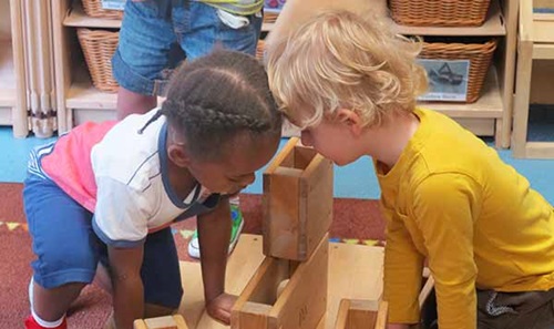 two nursery aged children looking at a mini hollow block tower