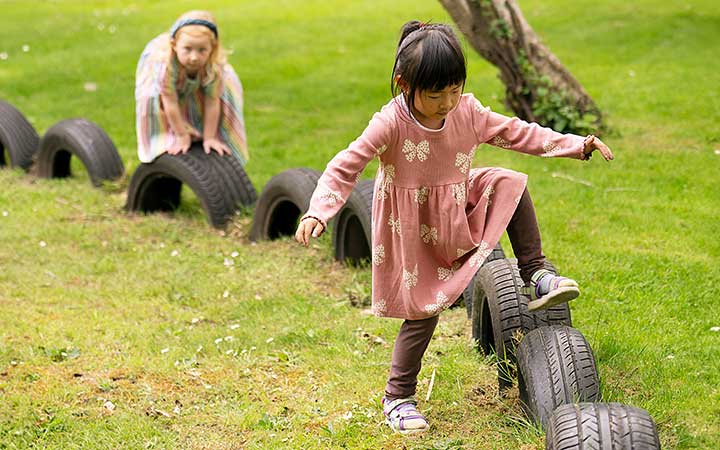 Two chldren in the nursery outdoor area balancing on tyres.