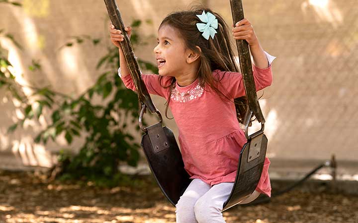 A girl playing on the swings in a nursery outdoor area.