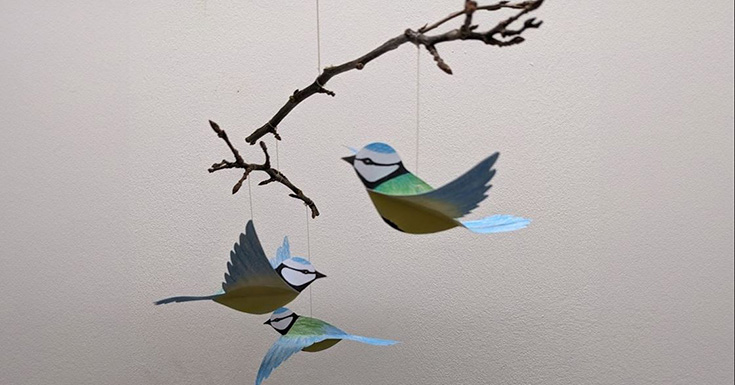 three paper blue tits hanging from branches