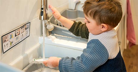 A boy washing a plate at the sink.