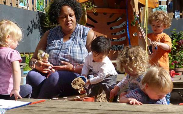 a teacher supervising toddlers playing in a sandbox