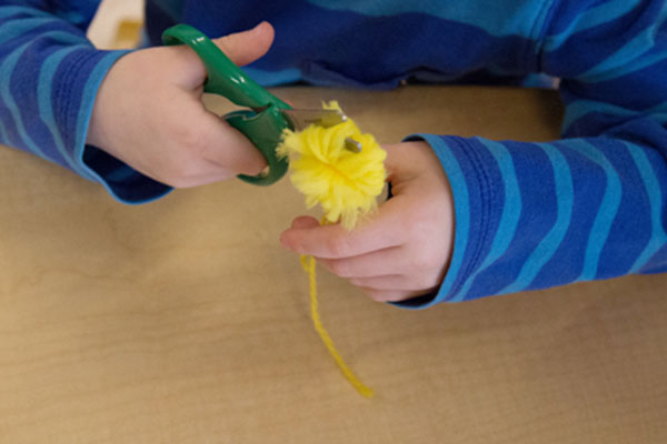 child cutting loops of yarn bundle to create pompom