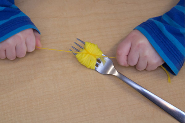 child's hands tying yarn around bundle of yarn