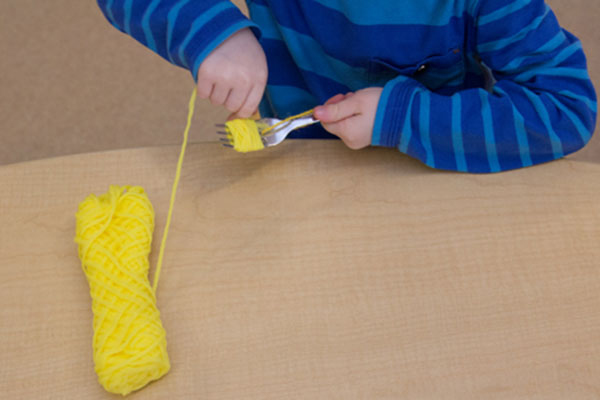child wrapping yarn around fork tines