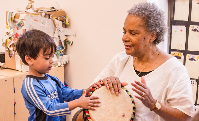 An early years teacher is showing a boy how to drum