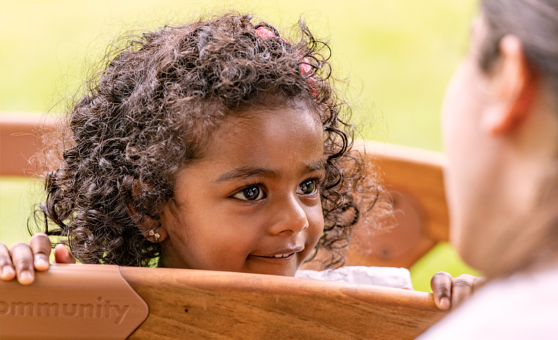 A kindergarten girl is looking at her teacher over the rail of a small bridge