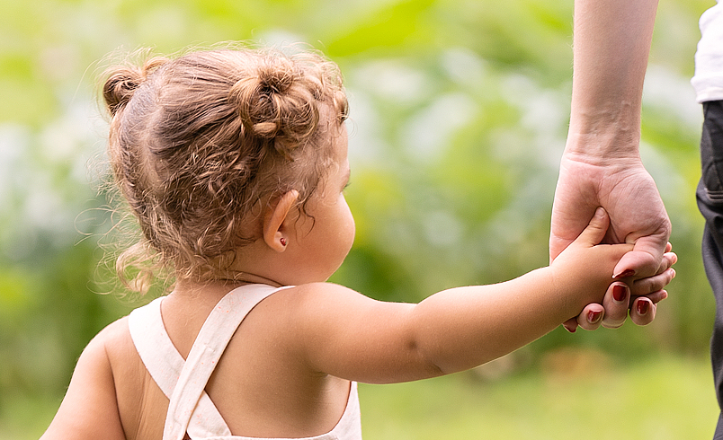 A toddler is holding the hand of an adult