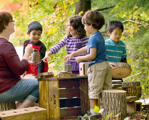 group of nursery aged children happily playing with found materials in the sandbox