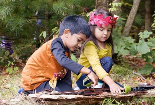 two nursery aged children sailing bark boats in a tiny pool of water