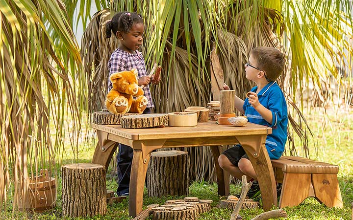 Two children engaged in role play at a table outdoors