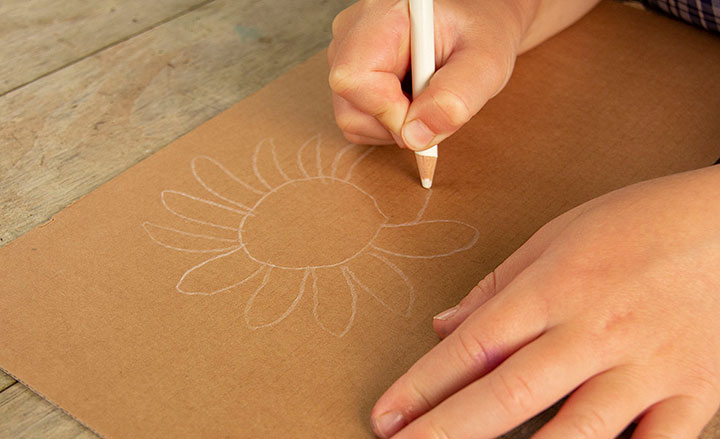 Child sketching flower on cardboard