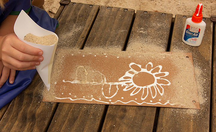 Sand being strewn over cardboard preparated with glue