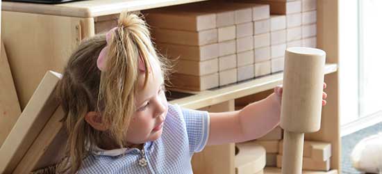 a nursery aged girl building a tower from unit blocks