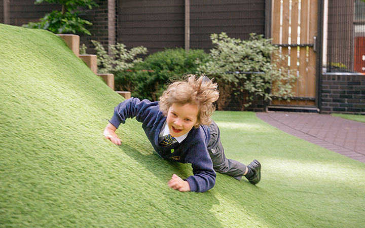 A smiling child rolling down a grassy hill at school playground during outdoor play.
