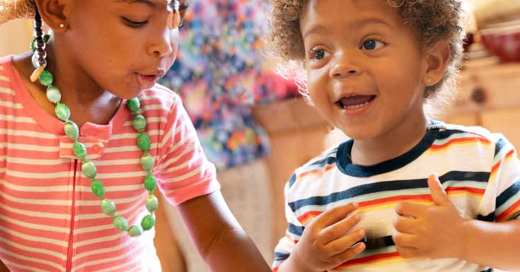 Closeup of two children laughing together as they play in the home corner