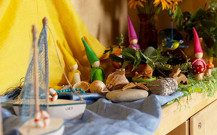 A nature-inspired display of wooden toys, felt gnome figurines fashioned around wooden peg dolls, small hand-made wooden boats, and decorative plants