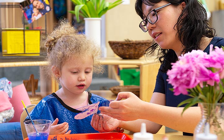 Child painting at table with teacher