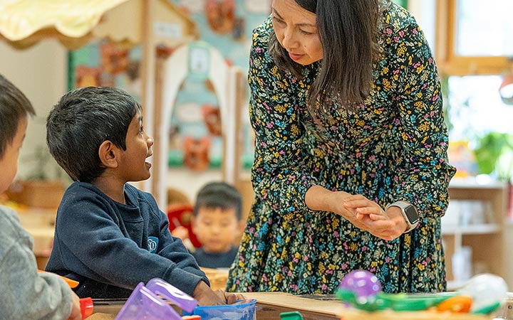 Boy at table interacting with teacher standing next to him