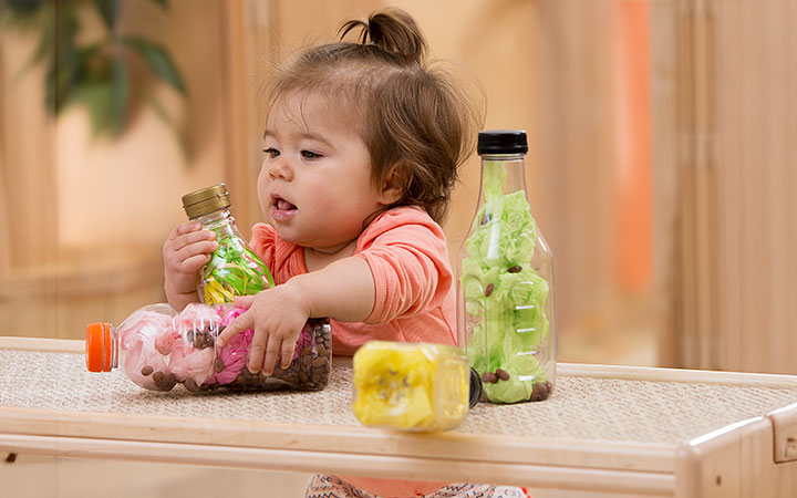 An infant reaching for coloured sensory shakers placed on a baby shelf