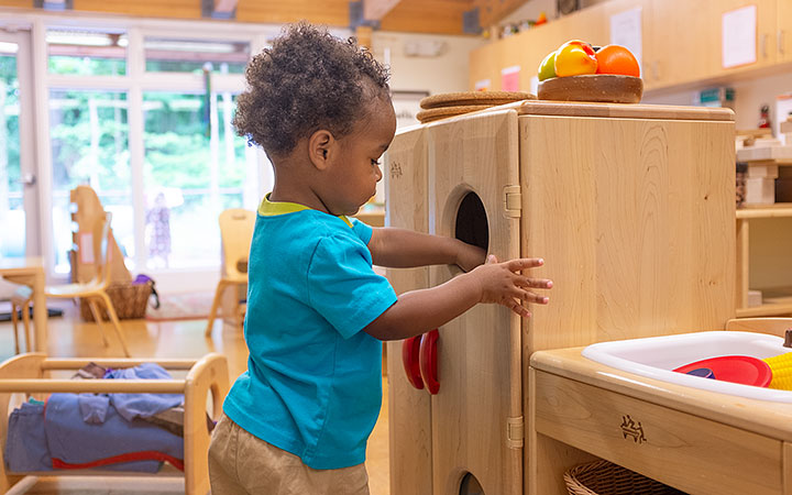 A toddler boy reaching his hand into a posting hole on play kitchen furniture