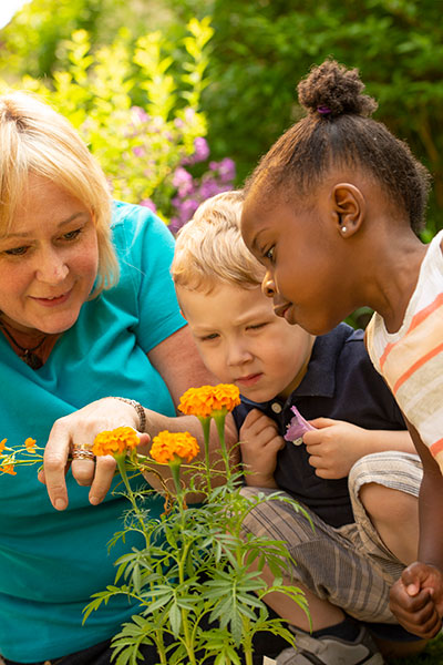 teacher and children looking closely at orange marigold flowers