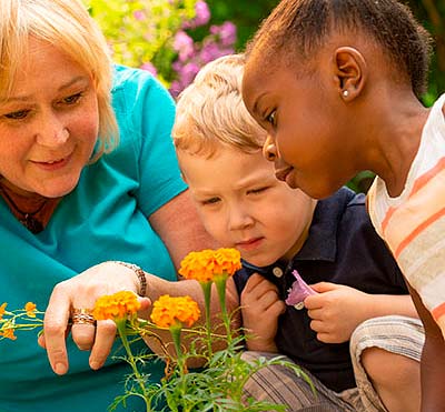 teacher and children looking closely at orange marigold flowers