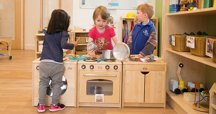 three children playing in a home corner of a nursery