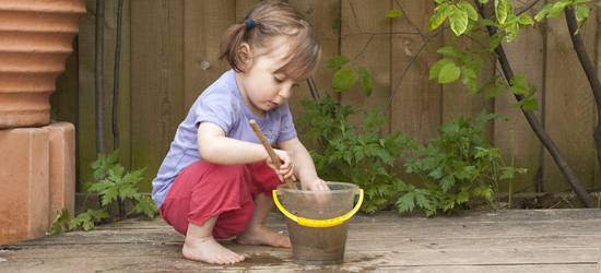 Girl stirring mud in a small bucket