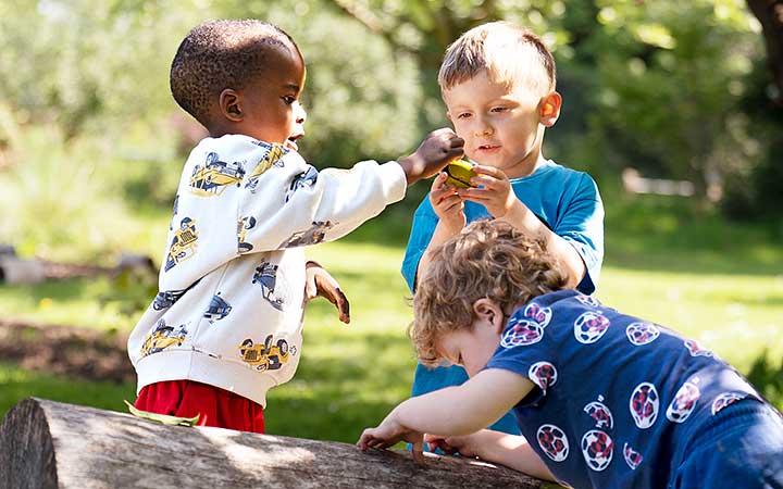 Three boys at a nursery playing outdoors near a log.