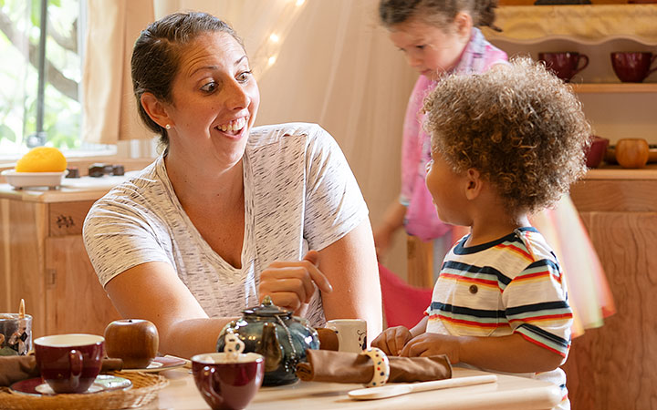 Preschool boy playing and looking at laughing teacher