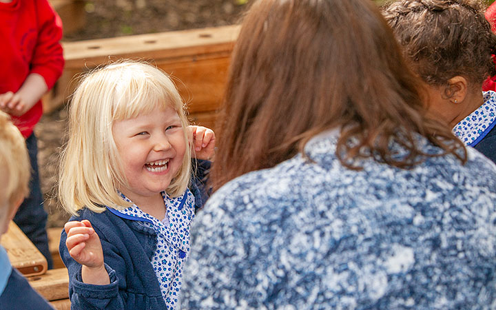 Toddler girl raising hands in air and lauging with teacher