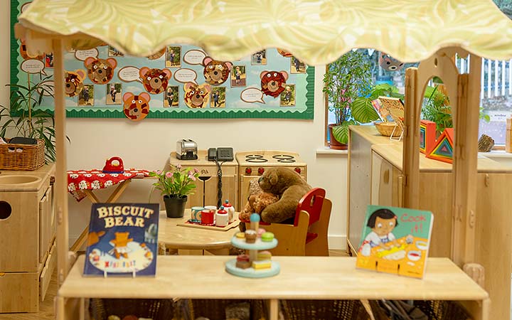 Indoor role play area with toy kitchen, books, and a teddy bear tea party setup.