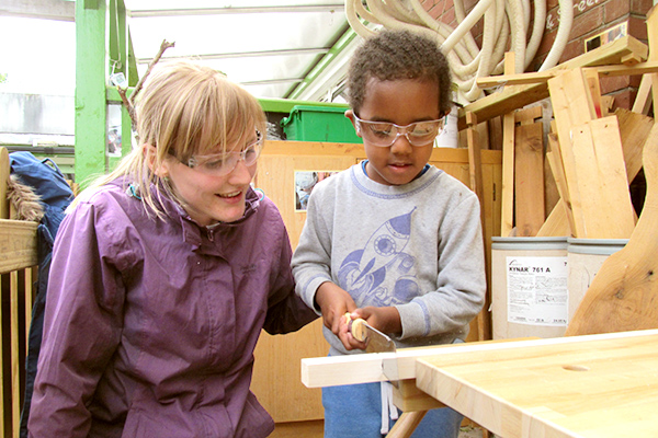 little boy sawing using the woodworking bench accompanied by a practitioner