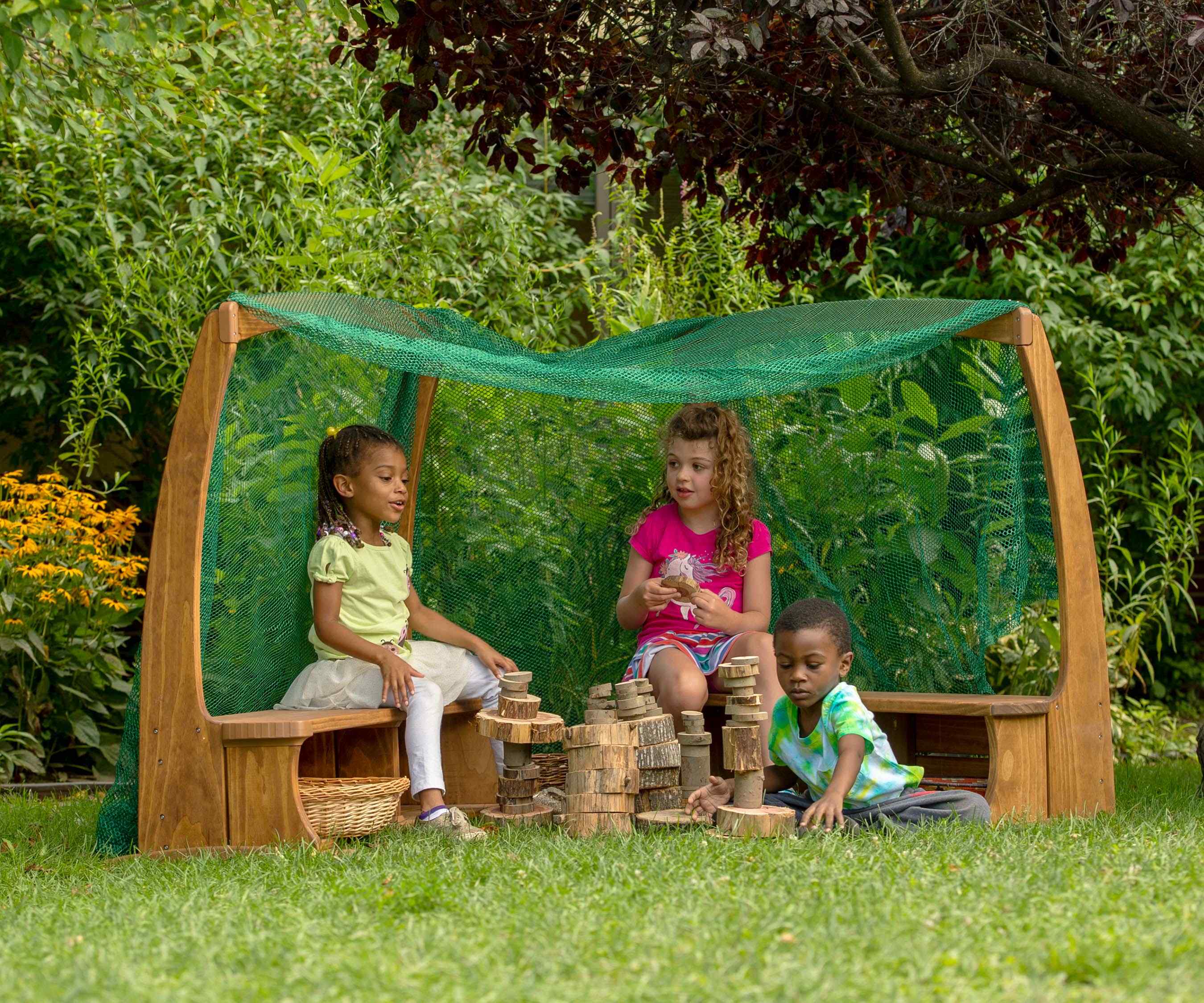 Three children playing with wooden blocks under a wooden Arbour with a green mesh roof.