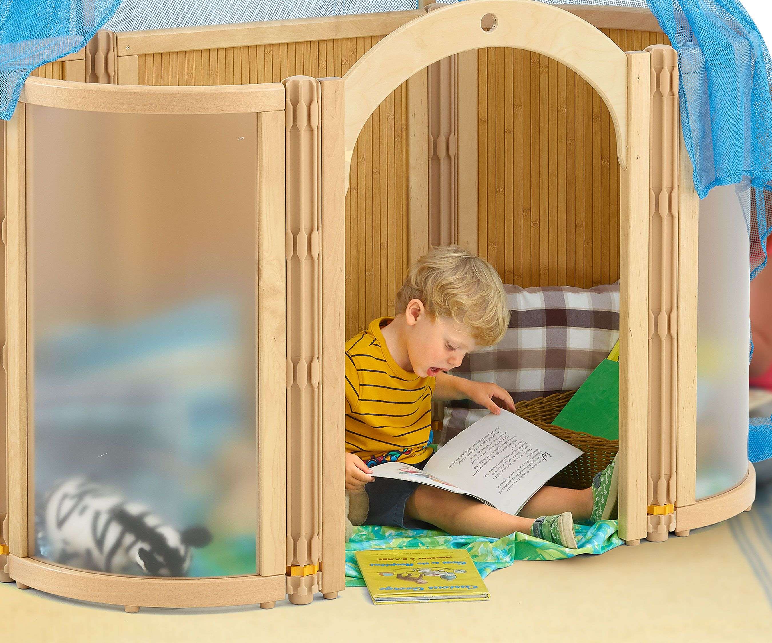 A young boy in a wooden playhouse with translucent walls and a blue mesh roof, reading a book.