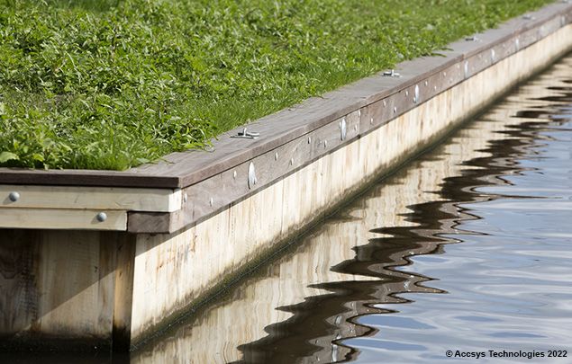 CanalLining: Wooden canal lining with green grass on top and water reflecting the structure below.