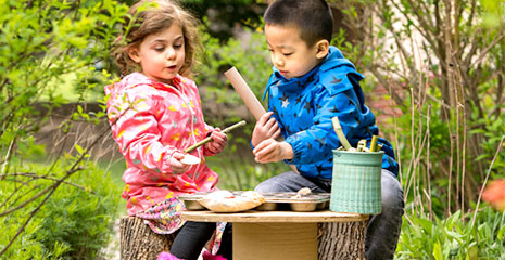 A boy and girl sitting outside at a table made from a wire reel