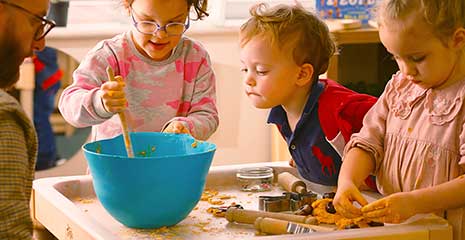 A teacher and three children experiment with dough on a discovery tray