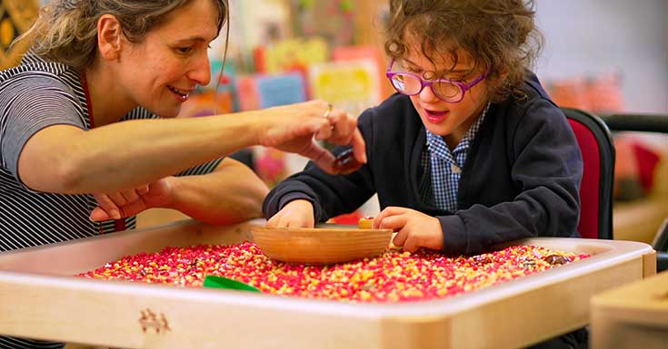 A teacher and a child with SEND do a sensory play activity on a play tray table