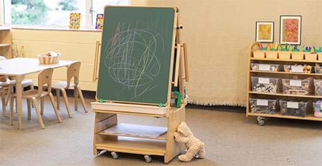 A teddybear is pushing an easel through a nursery room